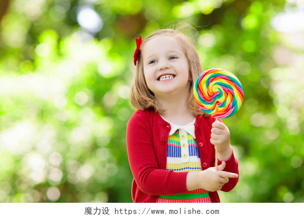 可爱的小女孩与七彩棒棒糖可爱的小女孩与大七彩的棒棒糖。孩子吃的甜糖果酒吧。年轻的孩子们的糖果。夏季户外的乐趣。学龄前孩子与糖棒棒糖。小吃在公园后学龄前的儿童.